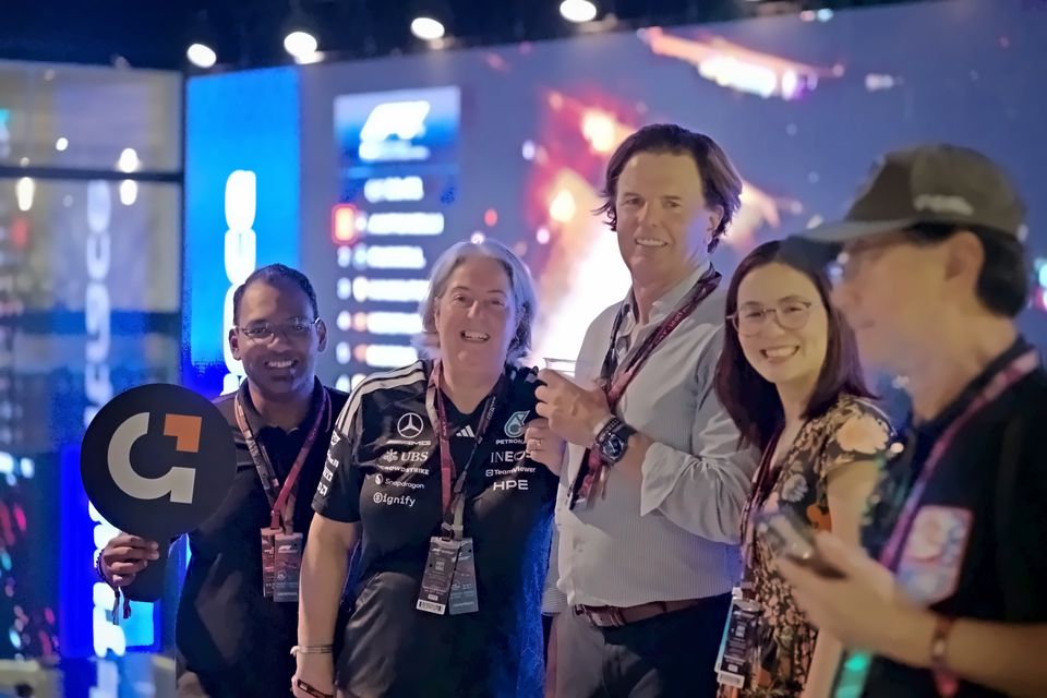 Guests in race weekend lanyards smile in front of a Formula 1 timing screen