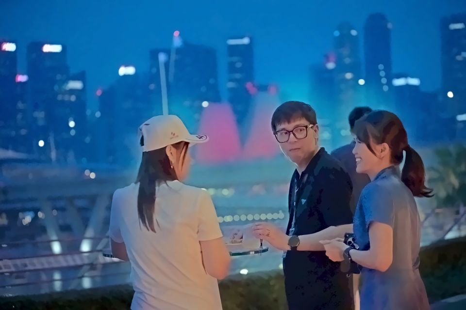 Guests talk on the lounge terrace at dusk, the Marina Bay skyline behind them