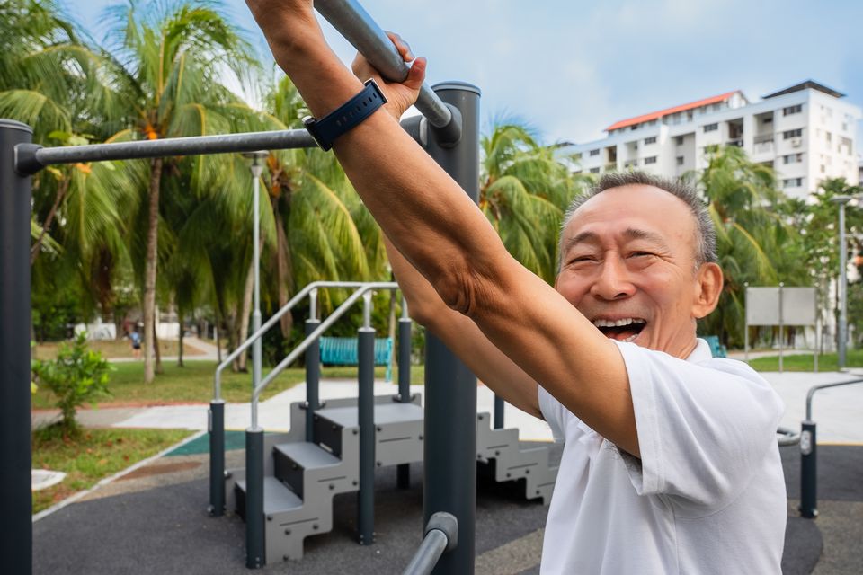A man laughs as he hangs from exercise bars in a Singapore park