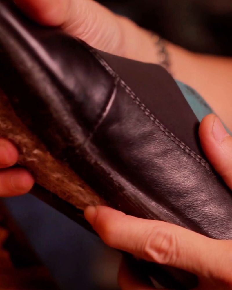 Hands shaping the leather of a shoe in a workshop