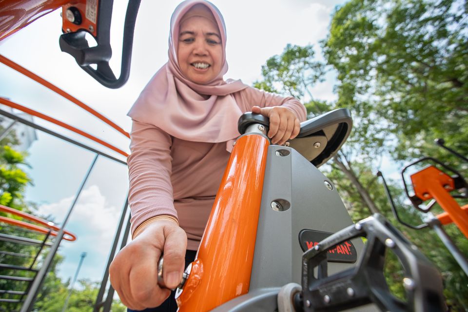 A woman in a pink hijab works out on orange fitness equipment, shot from below