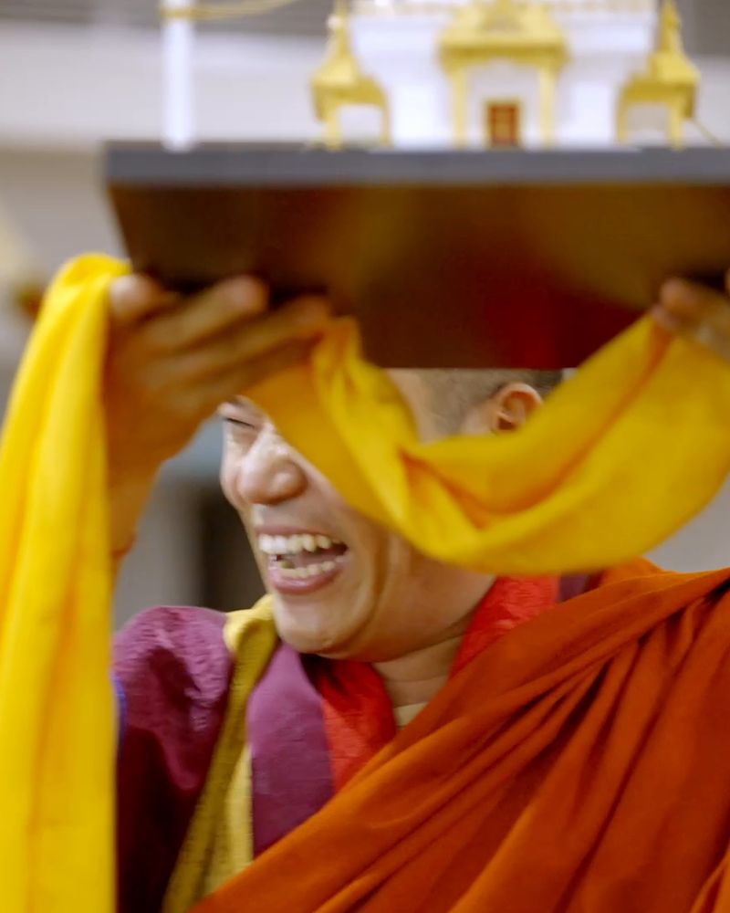 A monk laughs as he carries a stupa wrapped in yellow silk