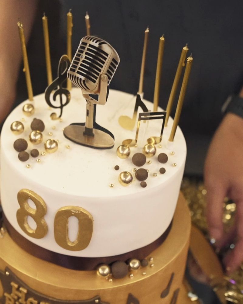 An 80th birthday cake with a microphone topper