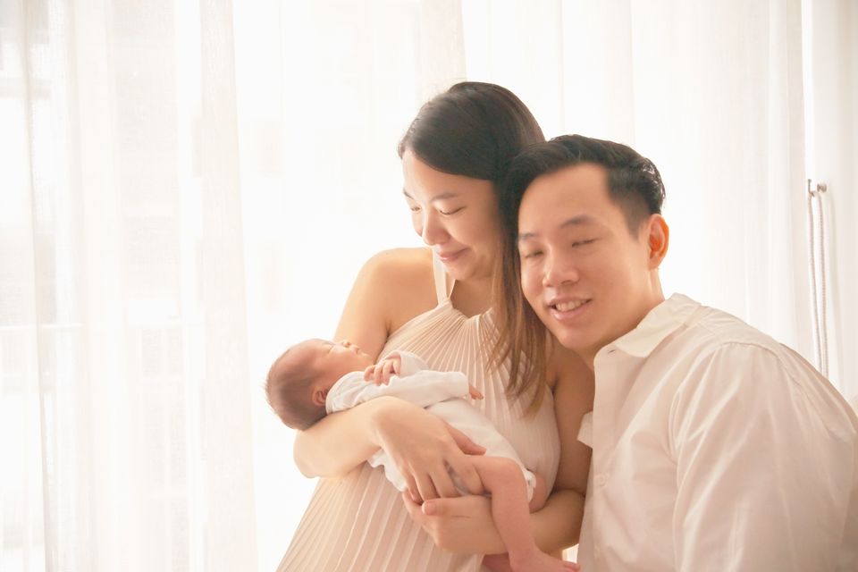 Mother and father laugh together on the bed with their newborn