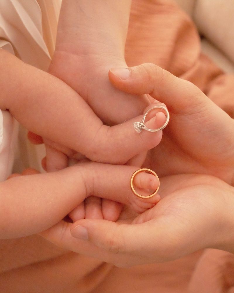 A newborn's hand held by her parents, wedding rings in view