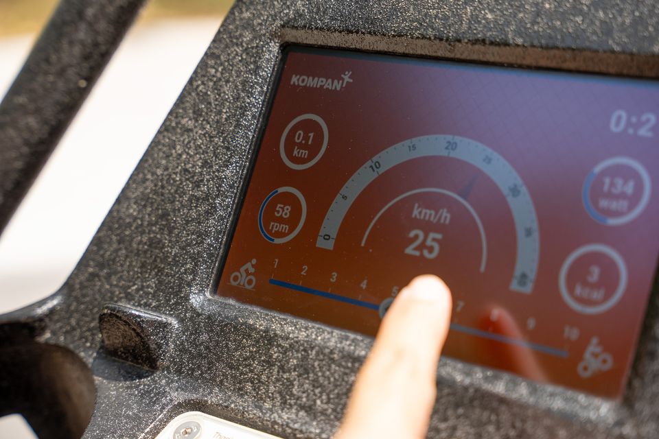 A finger taps the screen on a KOMPAN fitness station