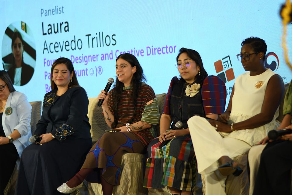Laura Acevedo Trillos speaks with her name on the LED wall, between Doreen Odvina Malbas and Maggerose Carado, Sanara Bussue-Ugboh beside them