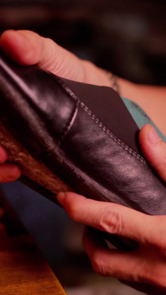 Hands work a piece of black leather on the workshop bench
