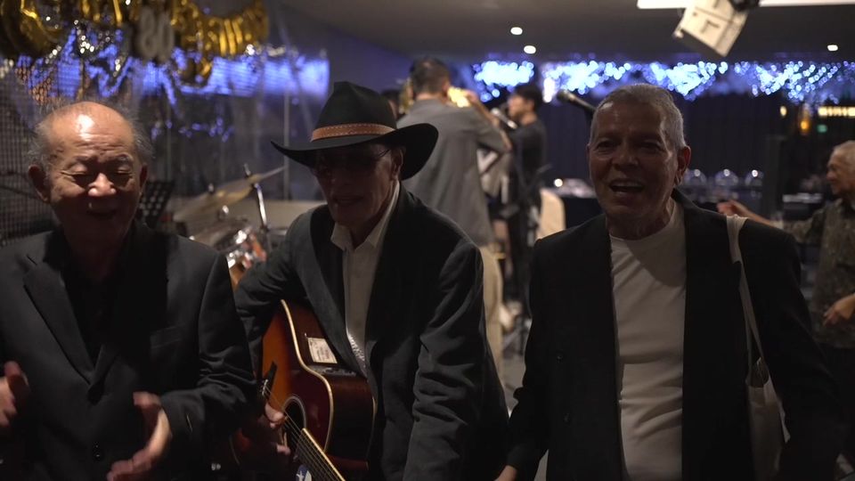 Old friends laugh and clap as a guitarist plays