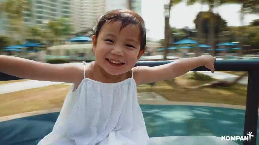 A small girl laughs as she spins on a playground roundabout