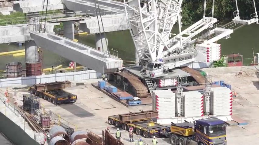 A crawler crane lifts a bridge beam over the Hougang site