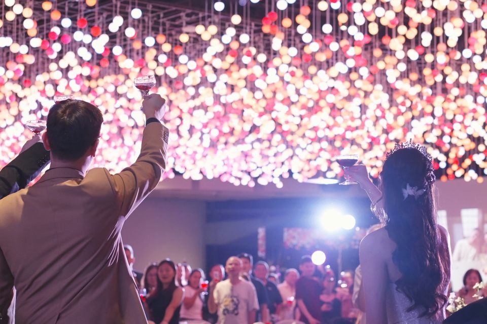 The couple raise a toast under hundreds of hanging lights